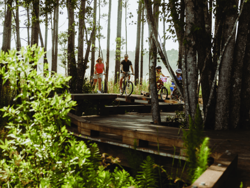 A family with two adults and two children rides bicycles along a wooden boardwalk through a forested area in the Wildlight Yulee Florida community.