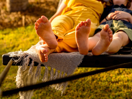 Two people relax on a hammock with bare feet visible, enjoying a sunny day and a fringed blanket underneath them, soaking in the peaceful vibe of the Wildlight Yulee Florida community.
