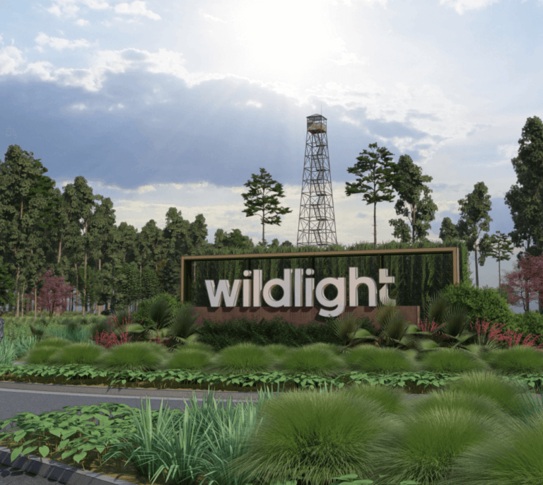 A landscaped entrance with a large "wildlight" sign, greenery, and an oil derrick structure under a partly cloudy sky welcomes you to the Wildlight Yulee Florida community.