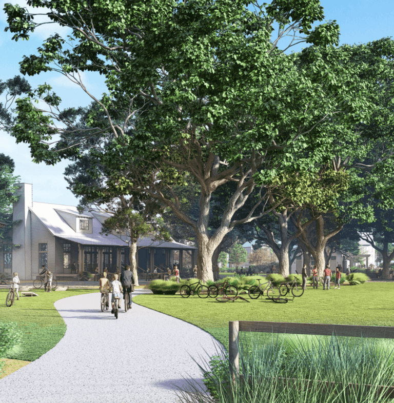 People walk and ride bicycles along a curved path beside a grassy lawn with large trees and a building in the background on a clear day, capturing the active lifestyle of the Wildlight Yulee Florida community.