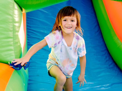 A young child with medium-length brown hair smiles while climbing inside a colorful inflatable play structure, enjoying family fun in the vibrant Wildlight Yulee Florida community.