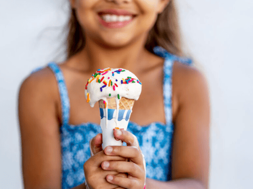 A smiling child in a blue patterned dress holds an ice cream cone with vanilla ice cream and colorful sprinkles in the vibrant Wildlight master planned community.