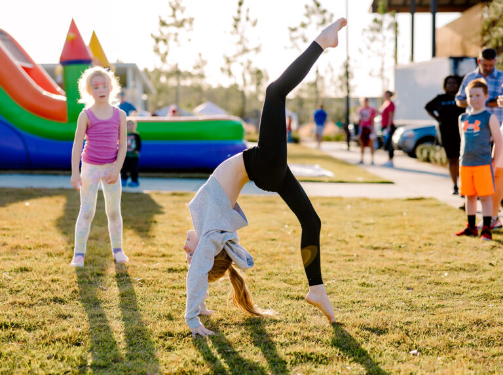 A child does a cartwheel on grass at an outdoor event in the Wildlight Yulee Florida community, with other children and an inflatable structure in the background.