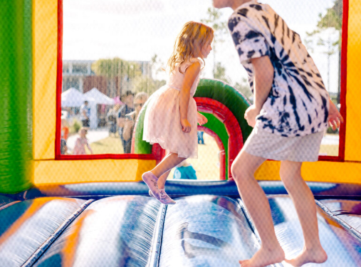 Two children jump inside a colorful inflatable bounce house at an outdoor event in the Wildlight Yulee Florida community, with tents and people visible in the background.