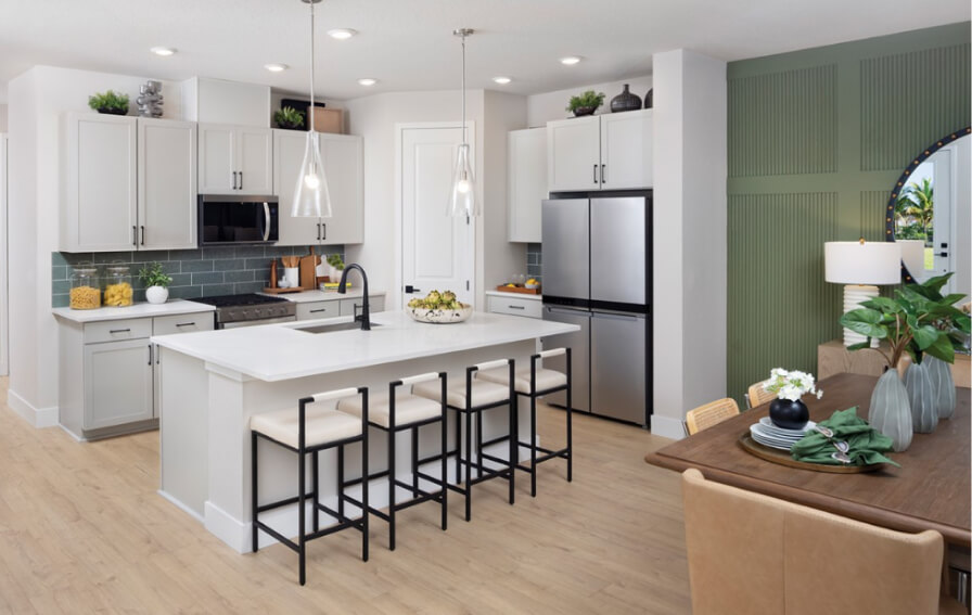 Modern kitchen with white cabinets, stainless steel appliances, an island with four stools, and a dining area set for four—perfect for entertaining in the sought-after Wildlight master planned community.