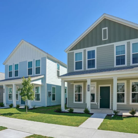 Two modern, two-story homes in Nassau County, Florida feature green lawns, large windows, and inviting front porches—side-by-side beneath a clear blue sky.