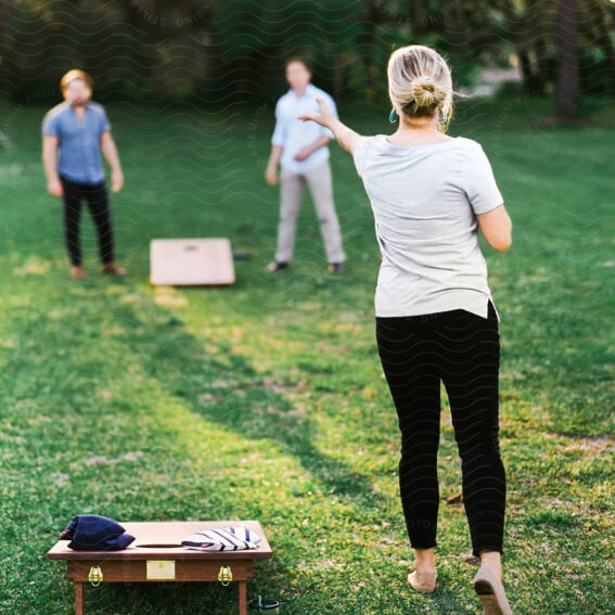 Three people playing cornhole on a grassy lawn in the Wildlight master planned community; one tosses a bean bag while two others stand by the boards, enjoying outdoor fun near new homes in Wildlight, FL.