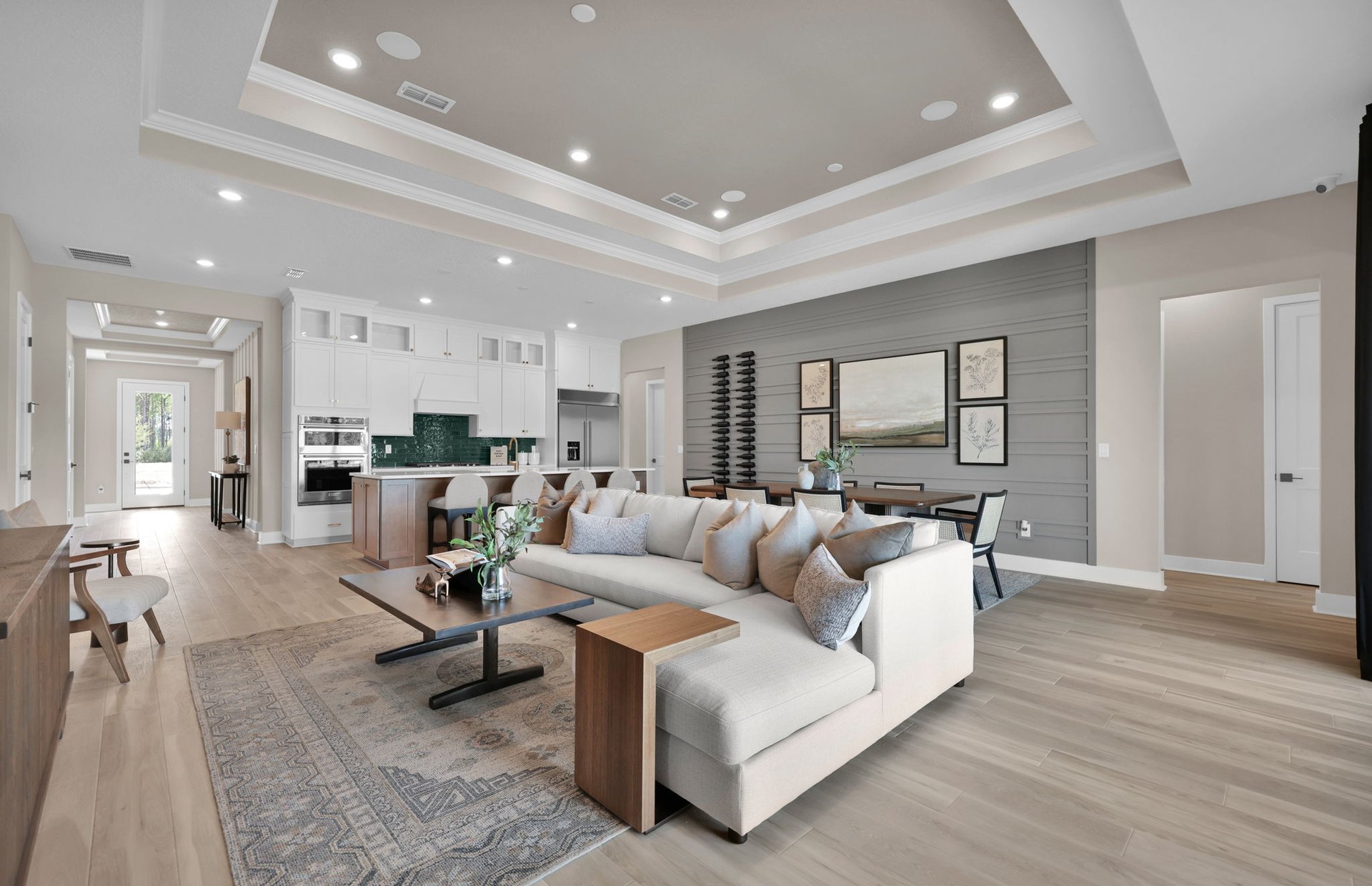 Modern open-concept living and dining area with light wood flooring, beige sectional sofa, large rug, and contemporary wall art—perfect for enjoying the vibrant lifestyle in the Wildlight Yulee Florida community. Kitchen is visible in the background.
