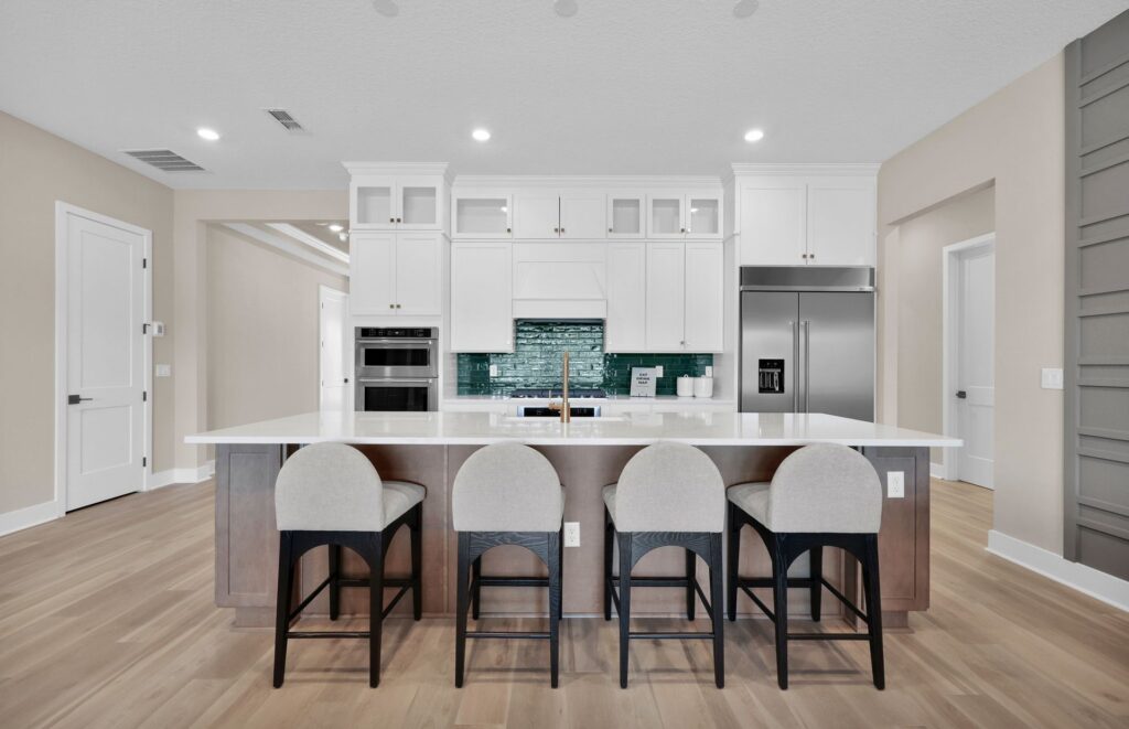 Modern kitchen in the Wildlight Yulee Florida community, featuring a large island with four chairs, white cabinets, stainless steel appliances, and light wood flooring.