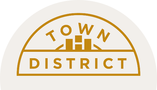 A gold outlined logo with the words "TOWN DISTRICT" and a simple cityscape graphic in the center on a light background, reflecting the spirit of the Wildlight Yulee Florida community and new homes in Wildlight FL.