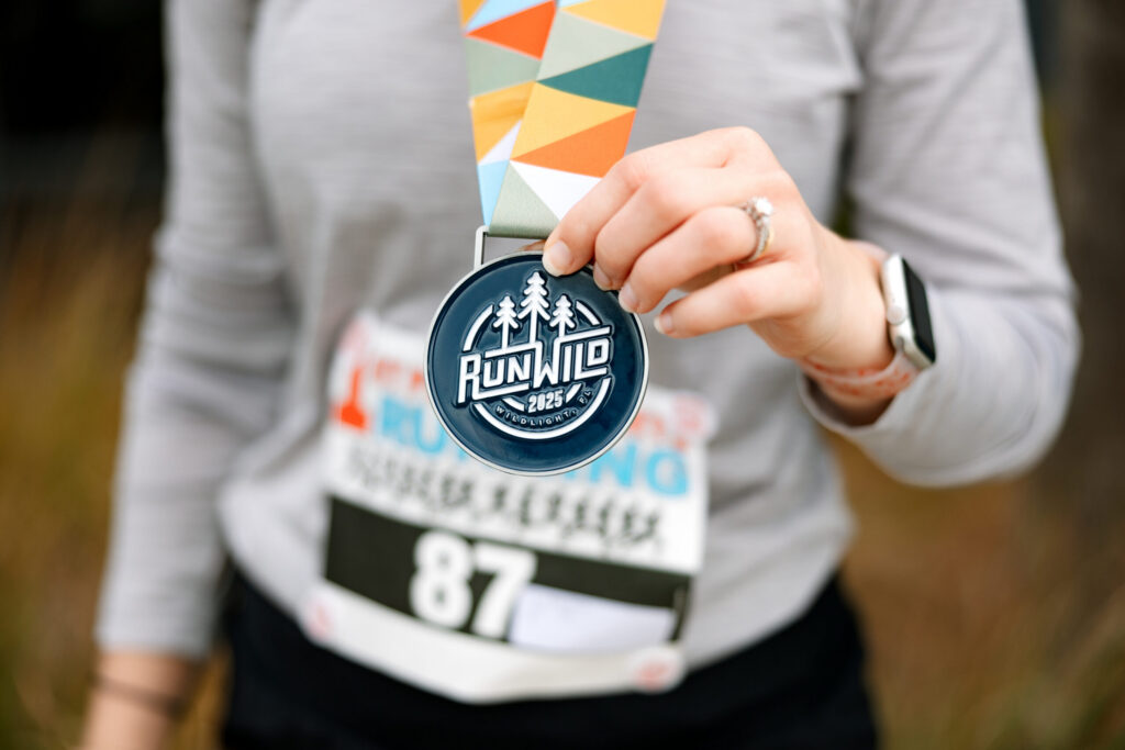 A person wearing a race bib numbered 87 holds up a "Run Wild 2023" finisher medal at the Wildlight master planned community in Nassau County, Florida.