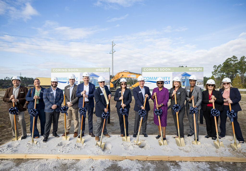 A group of people in business attire and hard hats stand in a row holding shovels at a groundbreaking ceremony for new homes in Wildlight FL, part of the vibrant Wildlight master planned community.