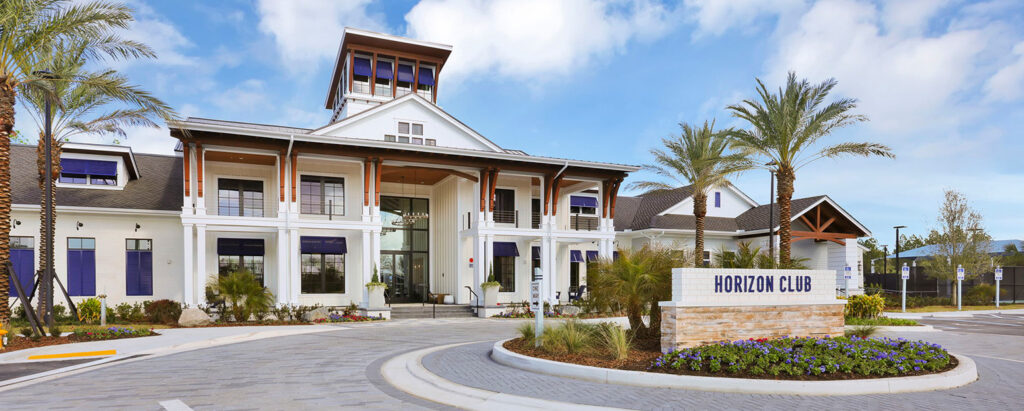 A large, modern building with columns and a glass entrance sits behind a sign reading "Horizon Club," surrounded by palm trees and landscaped grounds in the heart of the Wildlight Yulee Florida community.