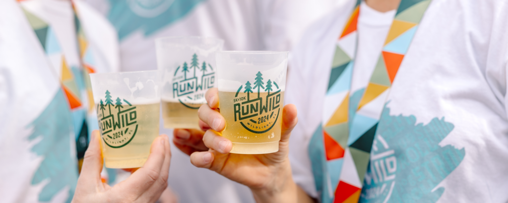 Three people in "Run Wild 2024" shirts and medals celebrate with a toast, highlighting the spirited Wildlight Yulee Florida community where new homes in Wildlight FL bring neighbors together for memorable moments.