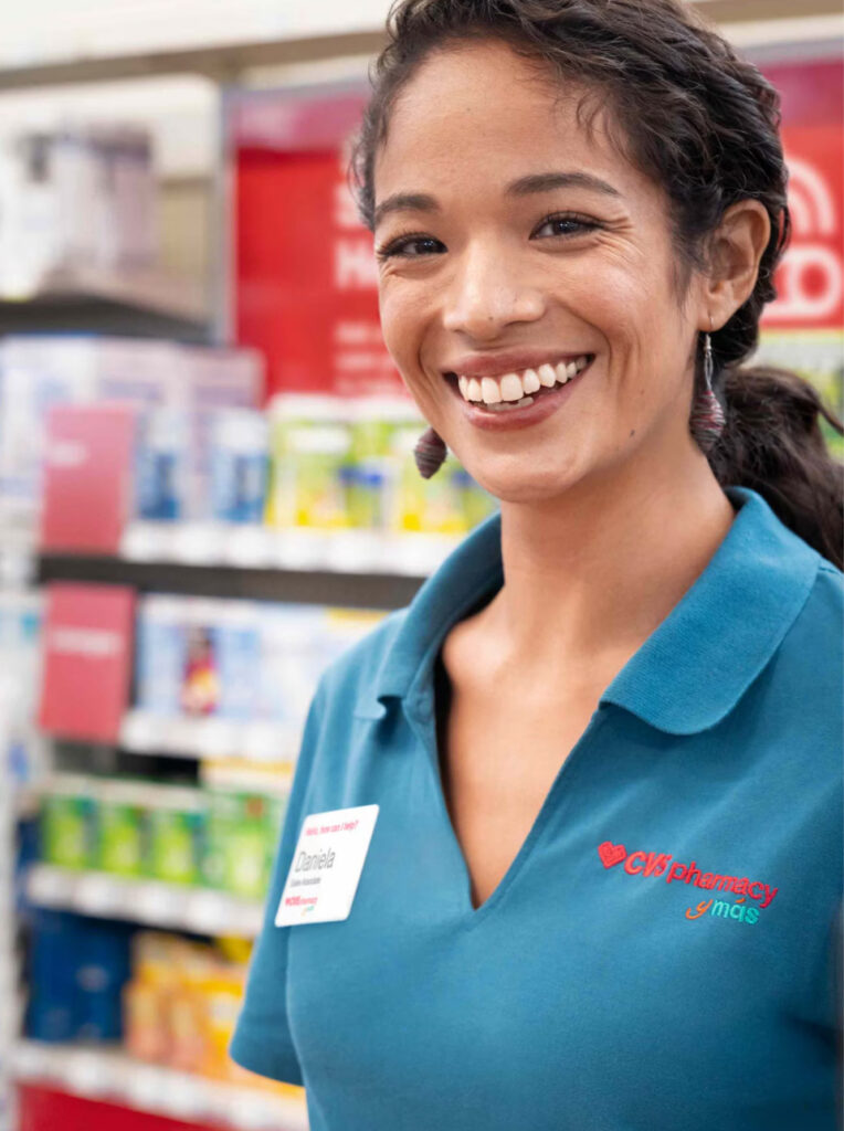 A smiling CVS pharmacy employee wearing a name tag stands in front of shelves, ready to assist the growing Wildlight Yulee Florida community within the vibrant Wildlight master planned community.