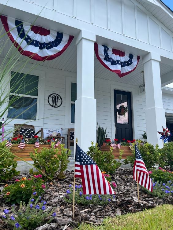 White house in the Wildlight Yulee Florida community, decorated with patriotic red, white, and blue bunting and multiple American flags displayed in the garden and on the porch.