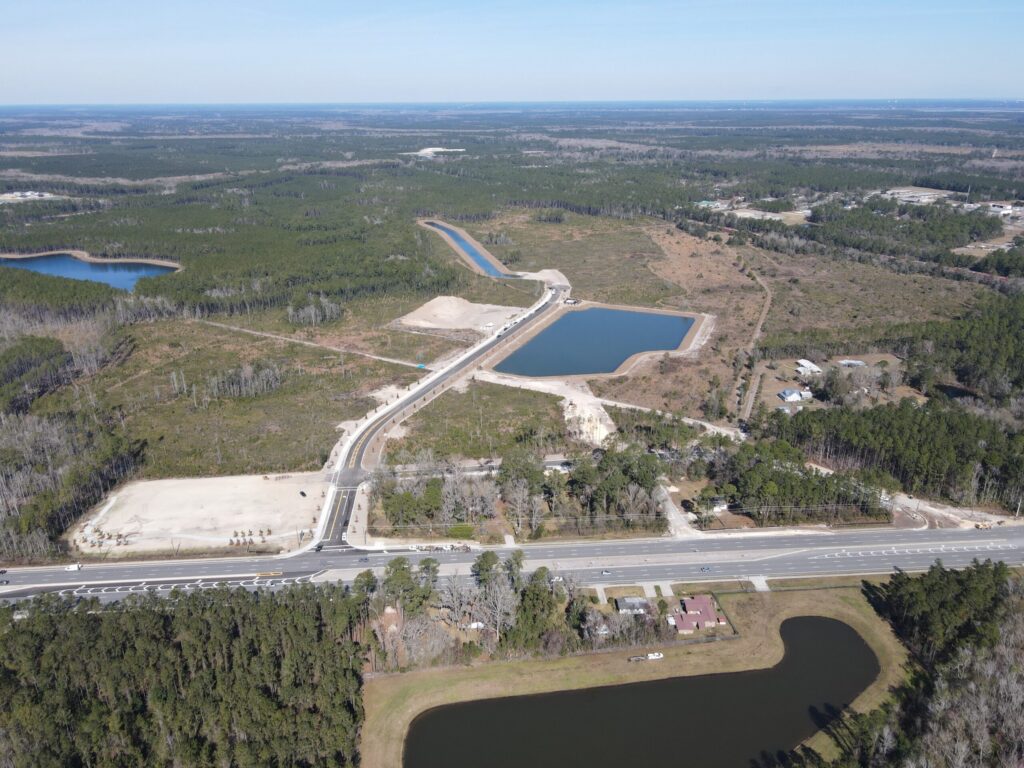 Aerial view of the Wildlight master planned community construction site with cleared land, roads, ponds, and surrounding forested areas under a clear sky.