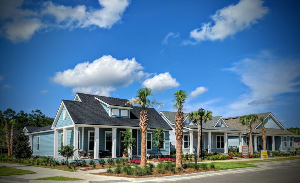 A row of modern, single-story blue houses with front porches and palm trees lines the landscaped yards beneath a bright sky—showcasing beautiful new homes in Wildlight FL, nestled in lovely Nassau County, Florida.