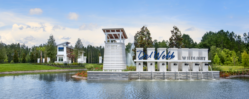Entrance sign for Del Webb Wildlight, a vibrant Wildlight Yulee Florida community, with modern structures surrounded by water, lush landscaping, and a backdrop of trees.