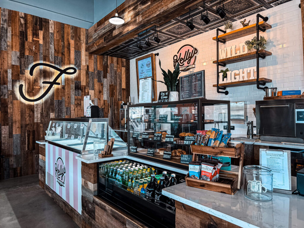A modern café counter with glass displays of pastries and drinks, a wooden wall with a neon "F", and a menu board on white subway tile, perfect for the vibrant Wildlight Yulee Florida community and those seeking new homes in Wildlight FL.