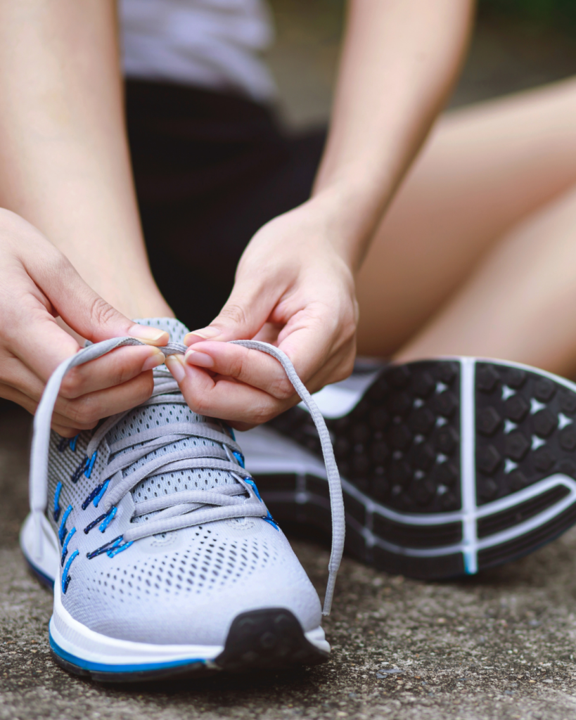 A person tying the laces of a gray athletic shoe while sitting on the ground, with the focus on their hands and shoes—perfectly capturing an active lifestyle in the Wildlight Yulee Florida community.
