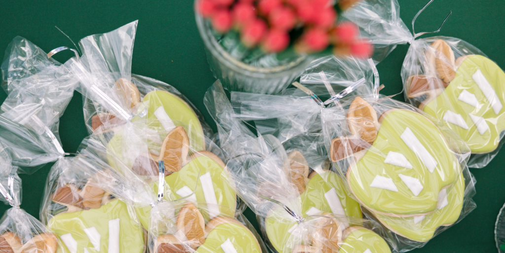 Individually wrapped green cookies with white decorations are arranged on a green surface next to a glass vase holding red flowers, capturing the festive spirit of the Wildlight Yulee Florida community.