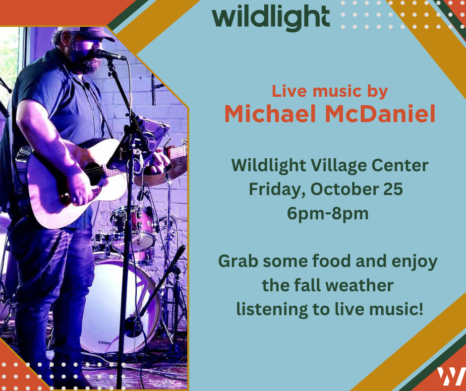 A man plays an acoustic guitar and sings into a microphone on stage; text promotes live music by Michael McDaniel at Wildlight Village Center in the heart of the Wildlight Yulee Florida community on Friday, October 25, 6–8pm.
