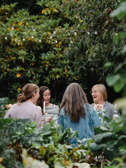 Four women sit around an outdoor table having a conversation, surrounded by greenery and string lights during daytime in the vibrant Wildlight Florida community.