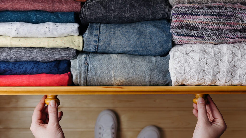 A person opens a wooden drawer filled with neatly folded clothes of various colors and textures, viewed from above—capturing the organized comforts found in new homes in Wildlight FL.