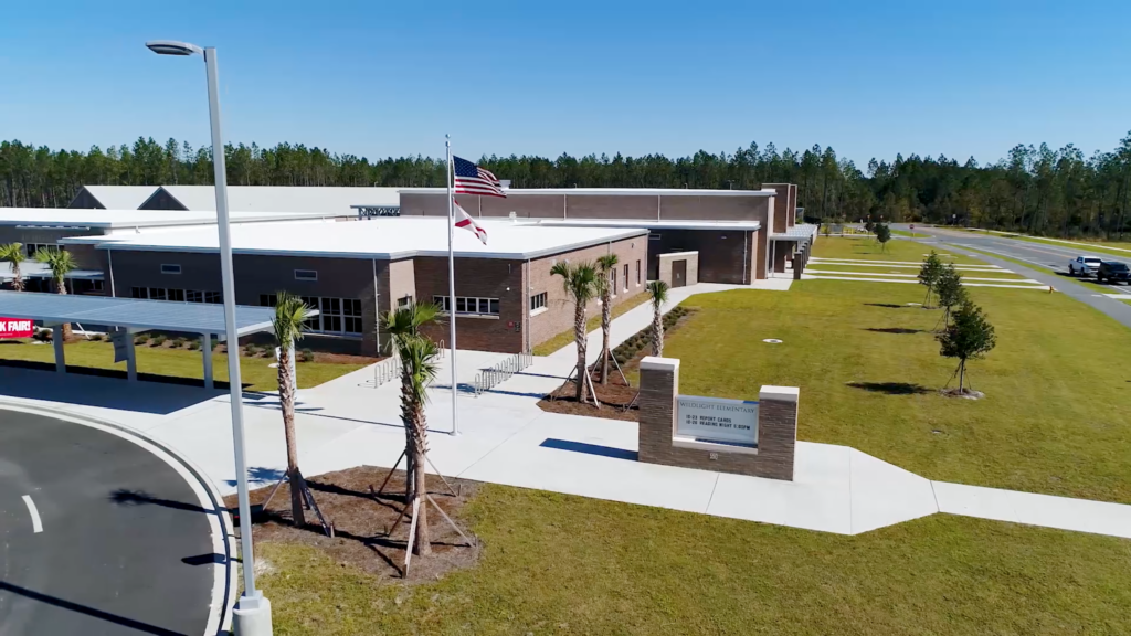 A modern brick school building with an American flag out front, surrounded by manicured lawns and young trees under a clear blue sky—perfect for families seeking new homes in Wildlight FL.