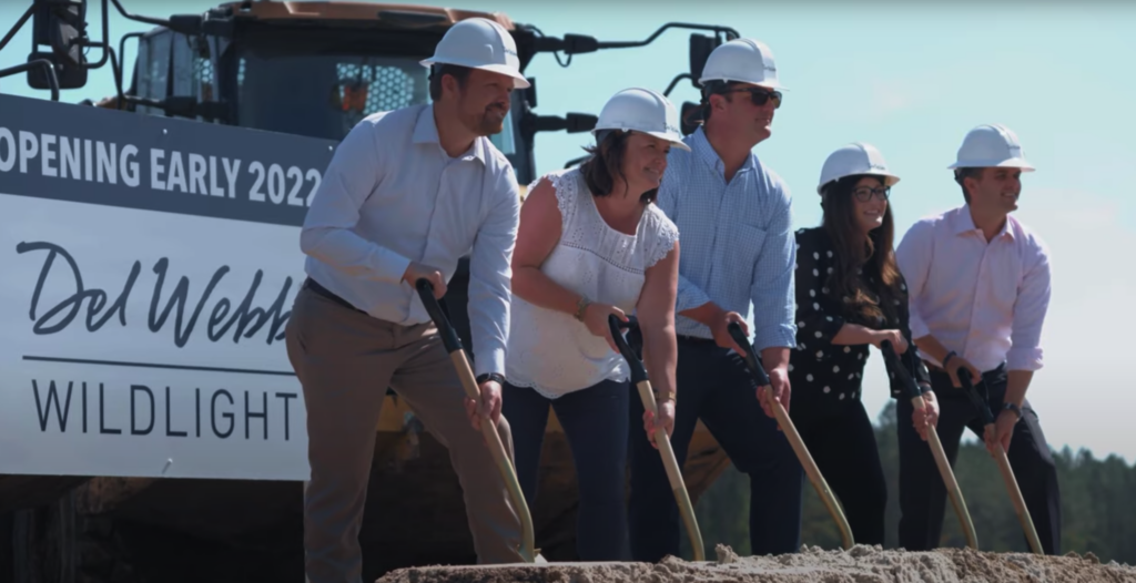 Five people wearing hard hats participate in a groundbreaking ceremony with shovels in front of a sign that reads "Del Webb Wildlight" and "Opening Early 2023," celebrating new homes in the Wildlight master planned community.