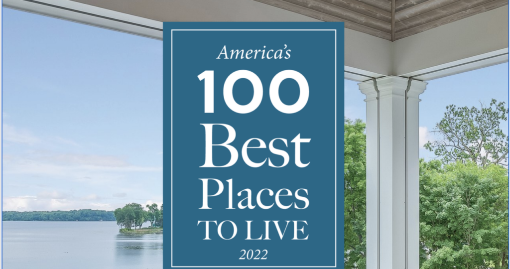 A blue sign reads "America's 100 Best Places to Live 2022" against a backdrop of a lake and green trees seen from a porch in the Wildlight Yulee Florida community.