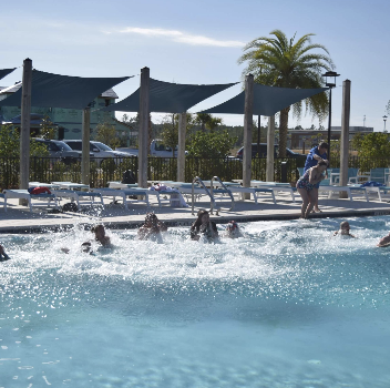 A group of people splash in a swimming pool while others relax by the poolside on a sunny day in the vibrant Wildlight Yulee Florida community.