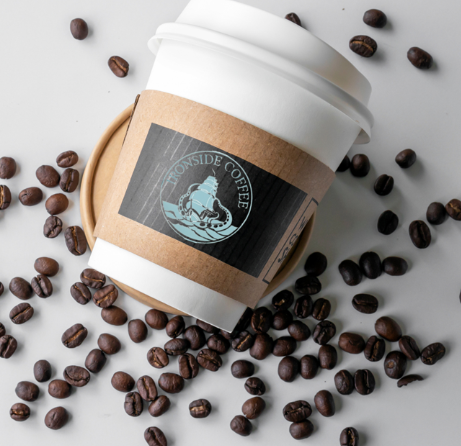 A disposable coffee cup with an "Ironside Coffee" label lies on its side, surrounded by scattered coffee beans—capturing a cozy morning vibe in Wildlight Florida, the heart of the Wildlight master planned community.