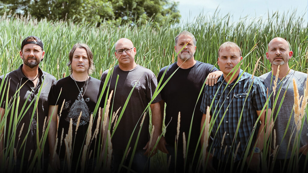 Six men standing in tall grass outdoors, posing for a group photo with trees and sky in the background in the vibrant Wildlight Yulee Florida community.