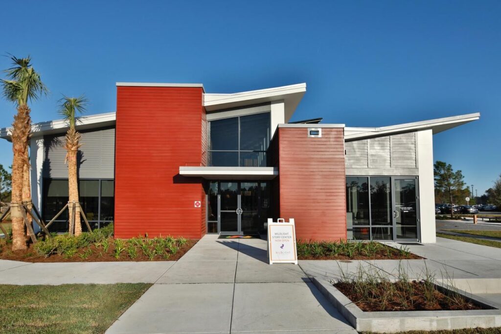 Modern building with red and white exterior panels, large windows, and a sidewalk leading to the entrance—reflecting the welcoming spirit of homes in Nassau County Florida. A sandwich board sign is placed near the front door.