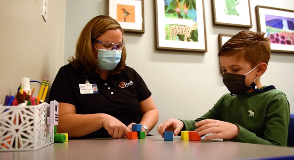 A woman and a boy, both wearing masks, sit at a table arranging colorful blocks in a bright room with animal pictures—a welcoming scene in the Wildlight master planned community in Wildlight Florida.