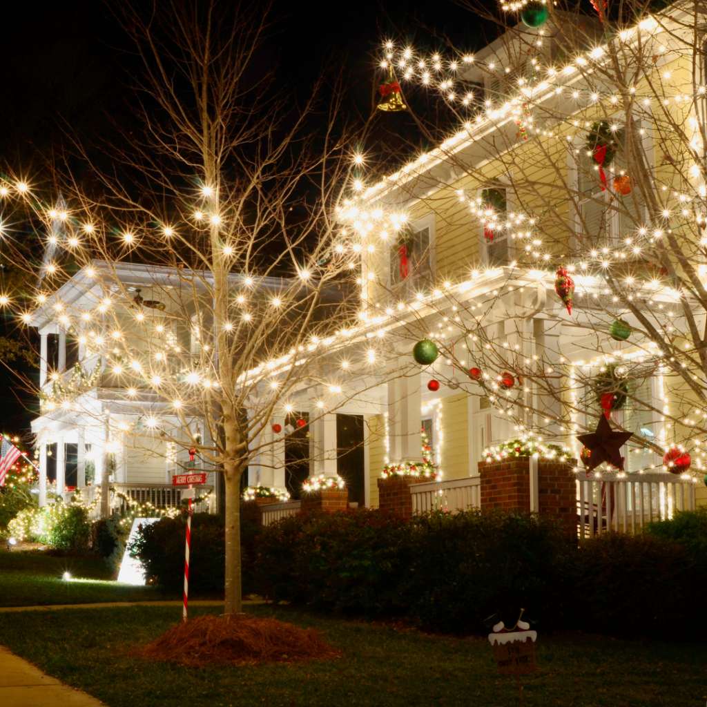 Two homes in Nassau County, Florida are decorated with white string lights and Christmas ornaments at night, with lights outlining the roofs, railings, and trees in the front yard.