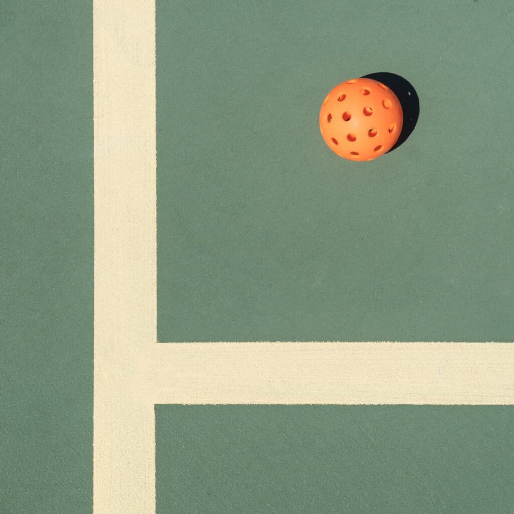 An orange perforated ball rests on a green court in the heart of the Wildlight Yulee Florida community, intersected by two wide cream-colored lines.