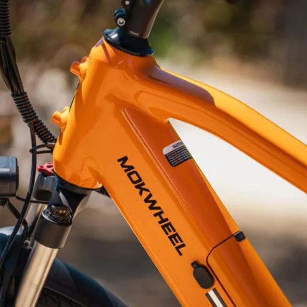Close-up of the front frame of an orange Mokwheel bicycle in Wildlight Florida, focusing on the brand logo and part of the handlebars and front suspension. Perfect for exploring trails near new homes in Wildlight FL.