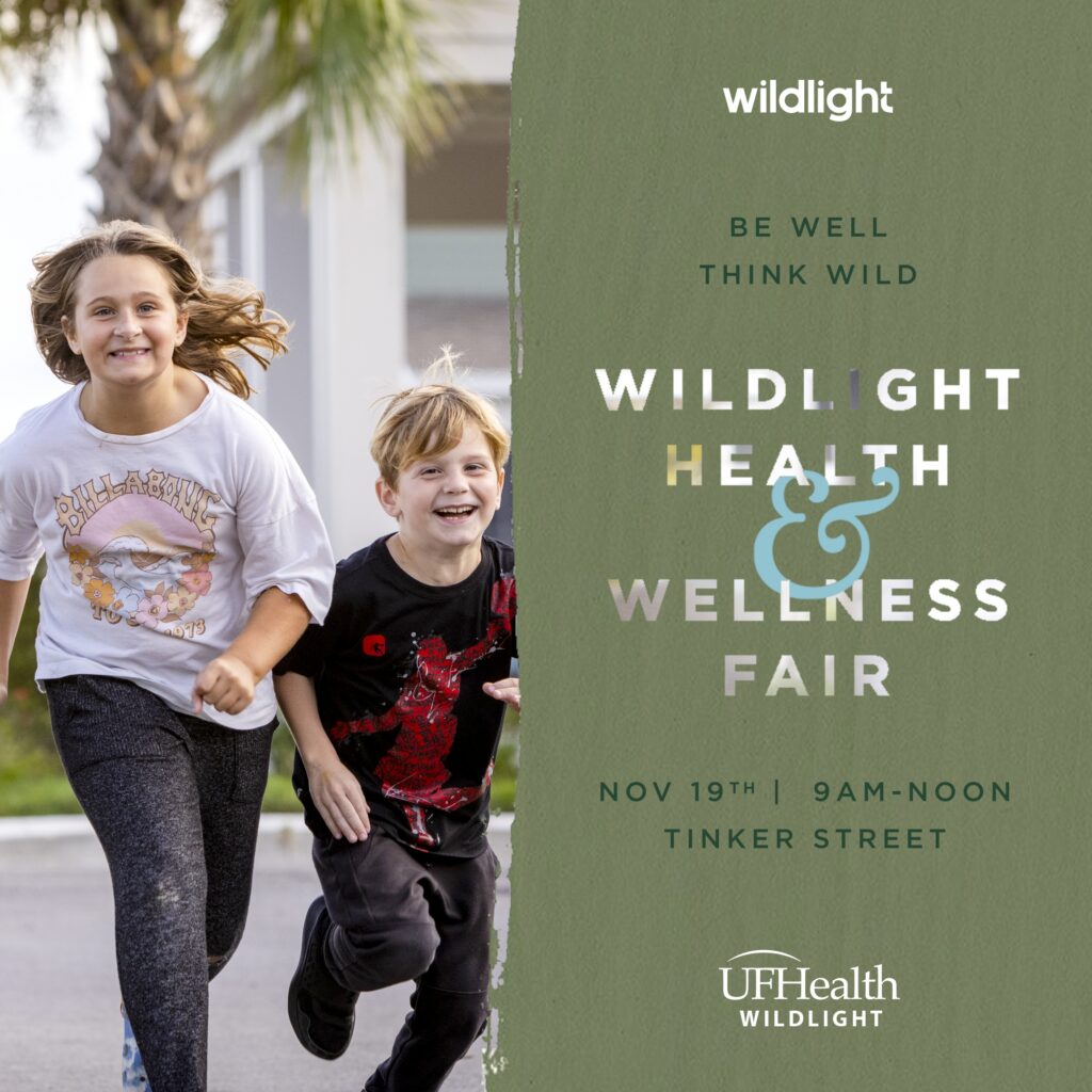 Two smiling children run outdoors next to a sign for the Wildlight Health & Wellness Fair, set for November 19th, 9am-noon, on Tinker Street—an exciting event in the vibrant Wildlight Yulee Florida community, hosted by UF Health Wildlight.