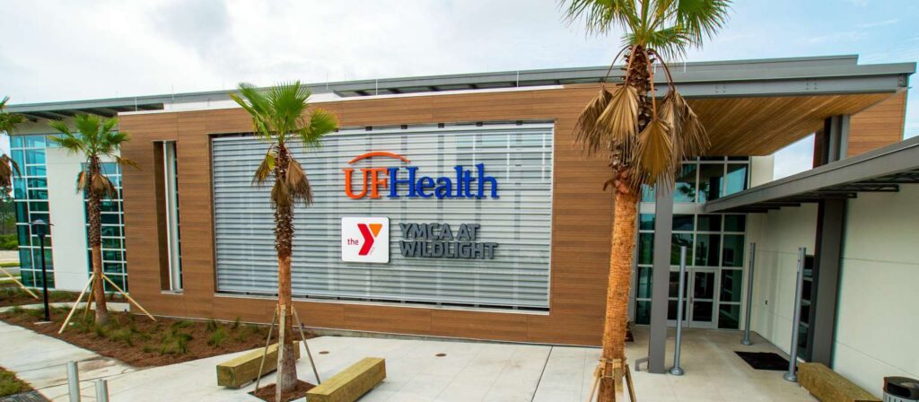 Exterior view of a building with UF Health and YMCA logos, surrounded by palm trees and modern architecture, showcases the vibrant spirit of the Wildlight Yulee Florida community within the Wildlight master planned community.