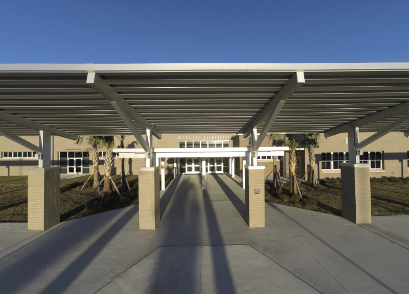 Covered walkway leading to the entrance of a modern brick building with "High School" above the doors, under a clear blue sky—an inviting scene in the heart of the Wildlight Yulee Florida community, known for beautiful new homes in Wildlight FL.