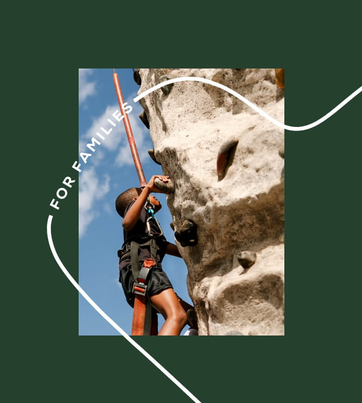 A child wearing a harness climbs an outdoor rock wall against a blue sky, with the words "FOR FAMILIES" on the image—capturing the active lifestyle found in new homes in Wildlight FL.
