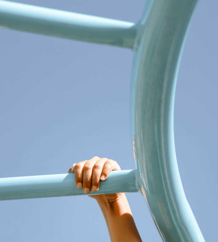 A person's hand grips a light blue metal bar on playground equipment against a clear blue sky, reflecting the vibrant energy found in new homes in Wildlight FL.