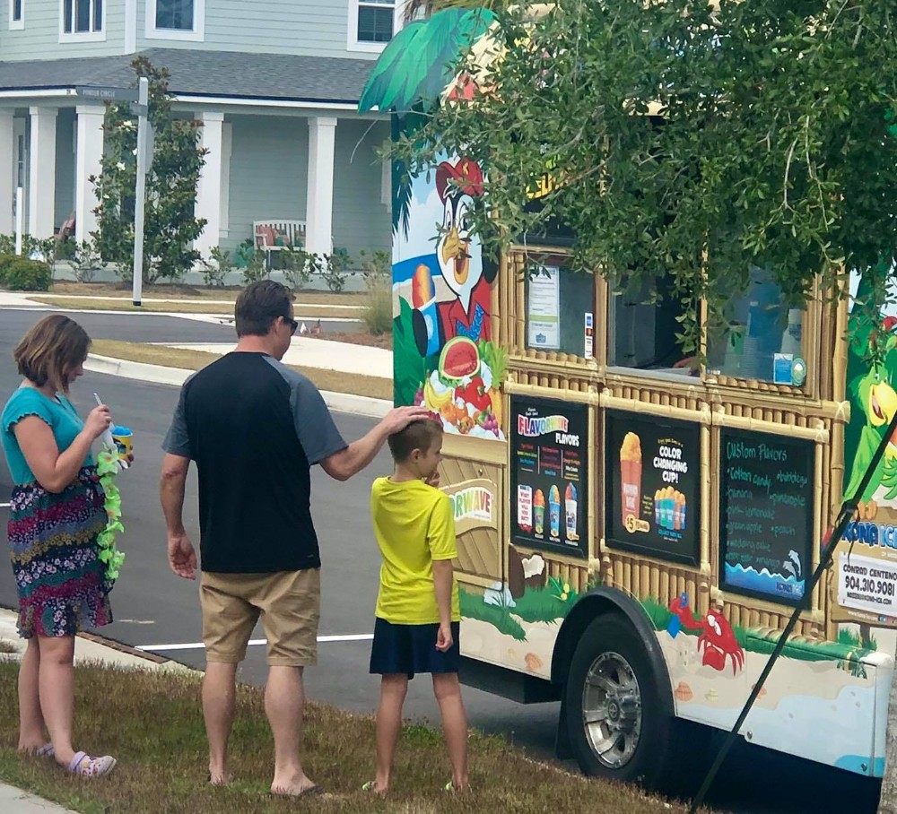 Three people, including two children and an adult, stand barefoot at a colorful food truck in the Wildlight master planned community, selecting treats—a perfect snapshot of vibrant life near new homes in Wildlight FL.