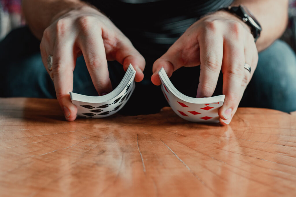 A person shuffling a deck of playing cards on a wooden surface, showing both hands bending the cards—perhaps unwinding after exploring homes in Nassau County, Florida or enjoying life at the Wildlight Yulee Florida community.
