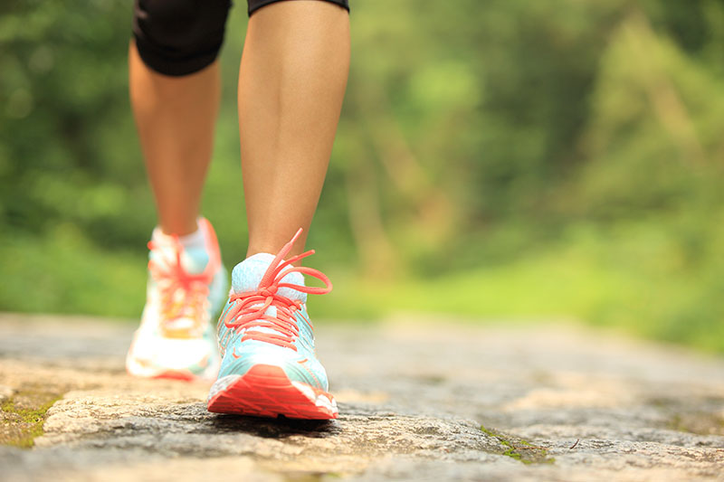 Person walking outdoors on a stone path in the vibrant Wildlight Yulee Florida community, wearing athletic shoes and cropped leggings, with lush greenery in the background.