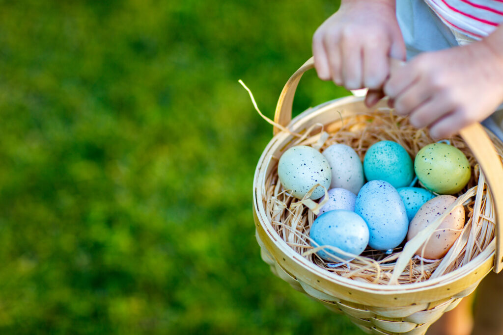 A person holds a wicker basket filled with speckled pastel-colored eggs on a grassy background, capturing the vibrant spirit of Wildlight Florida—a charming touch for those exploring new homes in Wildlight FL.