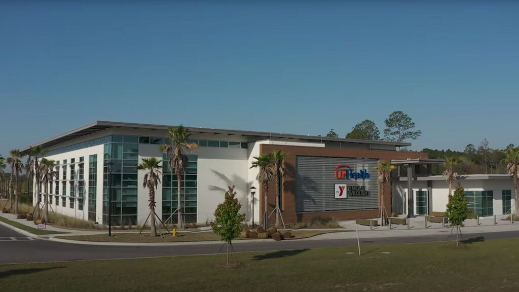 Modern building with glass and brick exterior, featuring UF Health and YMCA signs, surrounded by palm trees under a clear blue sky in the heart of the vibrant Wildlight Yulee Florida community.